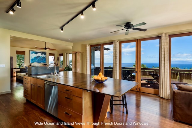 kitchen featuring a center island with sink, a water view, sink, and dark wood-type flooring