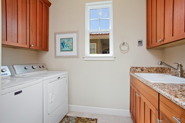 laundry area with cabinet space, light tile patterned floors, baseboards, washer and clothes dryer, and a sink