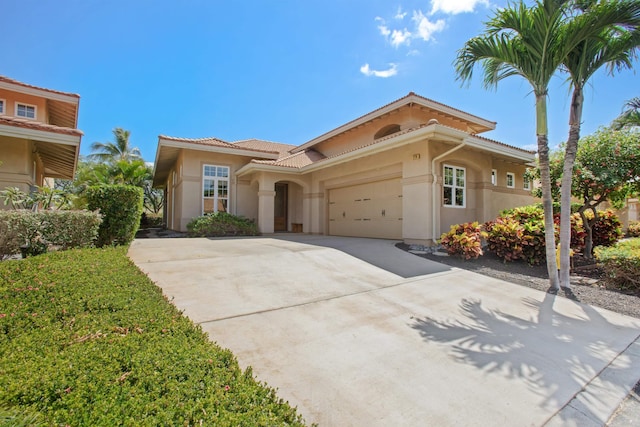 mediterranean / spanish house with a garage, driveway, a tiled roof, and stucco siding