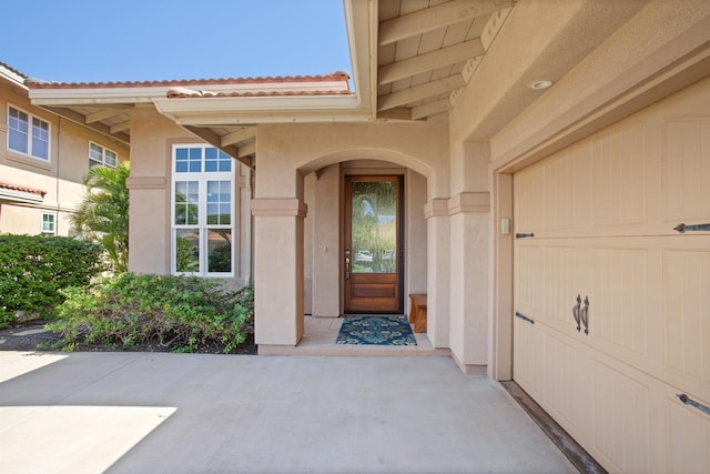 doorway to property with a garage, a tiled roof, and stucco siding