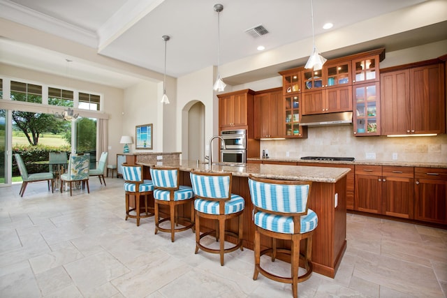 kitchen with under cabinet range hood, brown cabinetry, backsplash, and a kitchen breakfast bar