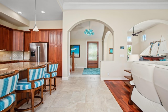 kitchen with baseboards, high end fridge, light stone countertops, tasteful backsplash, and crown molding