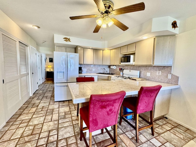 kitchen with white appliances, a breakfast bar area, a peninsula, a sink, and decorative backsplash