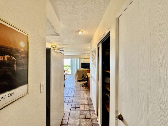 hall featuring stone tile floors, a textured ceiling, and a textured wall