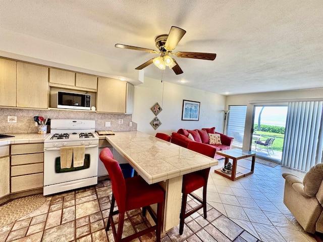 kitchen featuring light brown cabinets, open floor plan, decorative backsplash, a peninsula, and white appliances