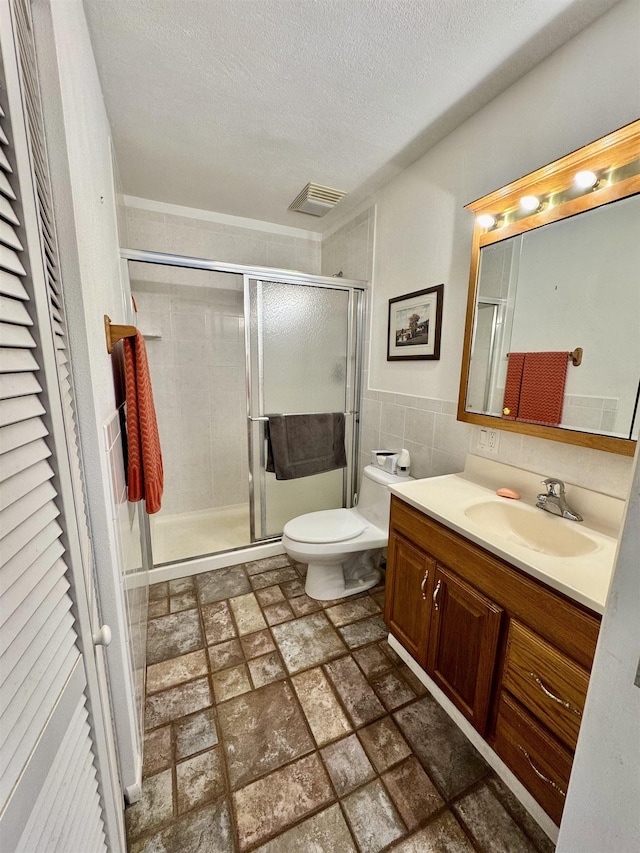 full bathroom featuring toilet, a textured ceiling, tile walls, a shower stall, and vanity