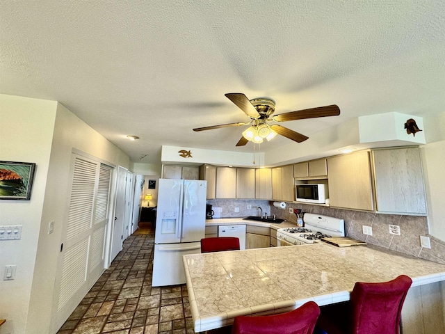 kitchen with a ceiling fan, a sink, backsplash, white appliances, and a peninsula