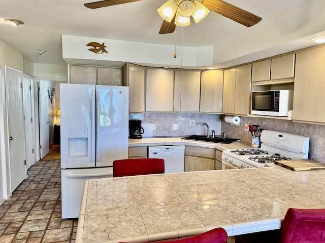 kitchen featuring white appliances, tile countertops, a peninsula, a sink, and tasteful backsplash