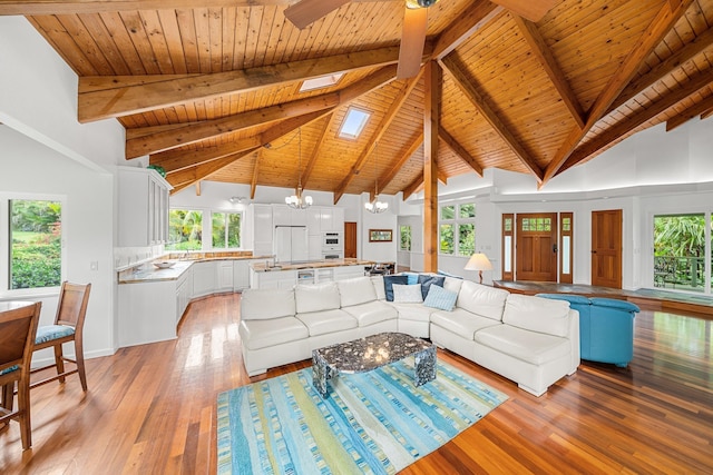 unfurnished living room featuring a skylight, high vaulted ceiling, a chandelier, beamed ceiling, and light hardwood / wood-style floors