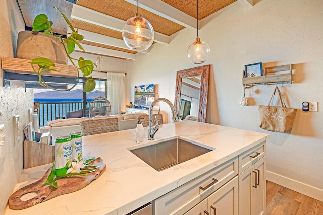 kitchen with sink, hanging light fixtures, light hardwood / wood-style floors, light stone countertops, and beam ceiling