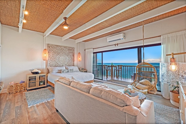 bedroom with an AC wall unit, hardwood / wood-style floors, access to outside, a water view, and beam ceiling