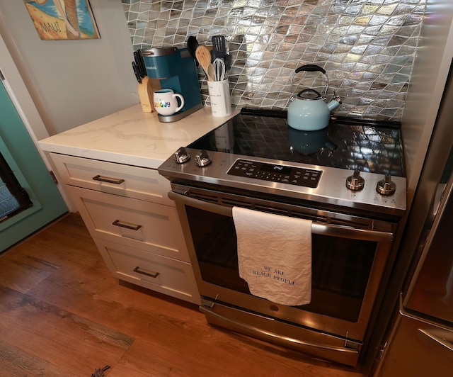 kitchen with tasteful backsplash, wood-type flooring, fridge, stainless steel electric stove, and white cabinets