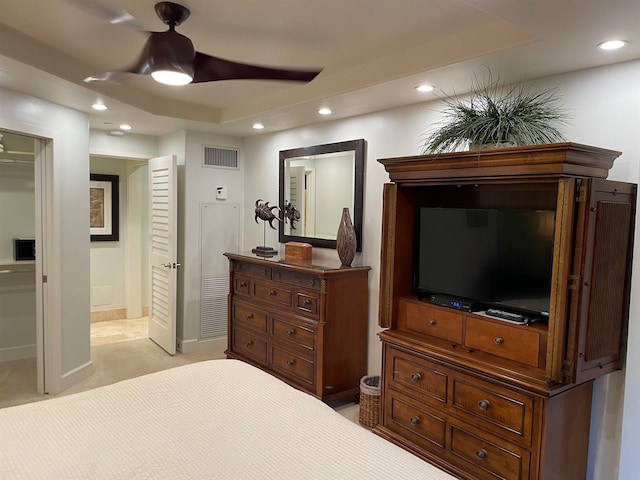 bedroom featuring a tray ceiling, light colored carpet, ensuite bathroom, and ceiling fan