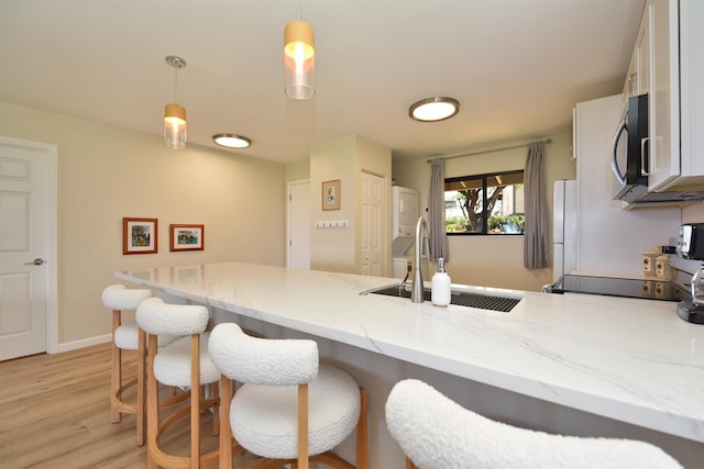 kitchen with light stone counters, white cabinets, light wood finished floors, a sink, and a peninsula