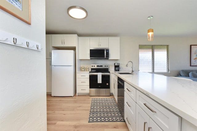 kitchen with a sink, light wood-style floors, white cabinetry, hanging light fixtures, and appliances with stainless steel finishes