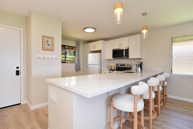 kitchen with stainless steel appliances, a breakfast bar area, light stone counters, a peninsula, and light wood-style flooring