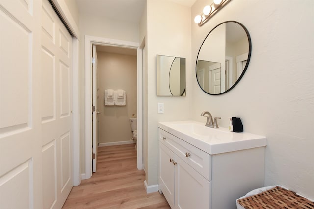 bathroom featuring baseboards, wood finished floors, toilet, and vanity
