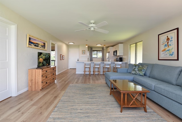 living area with ceiling fan, light wood-style flooring, and baseboards