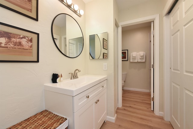 bathroom featuring toilet, vanity, wood finished floors, and baseboards