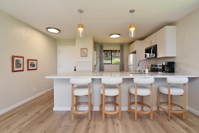 kitchen featuring white cabinetry, a sink, appliances with stainless steel finishes, light wood finished floors, and a peninsula