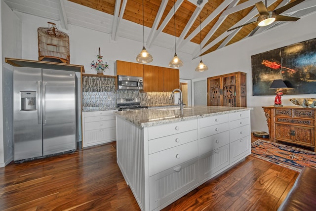 kitchen featuring stainless steel appliances, beam ceiling, light stone counters, a kitchen island with sink, and white cabinetry