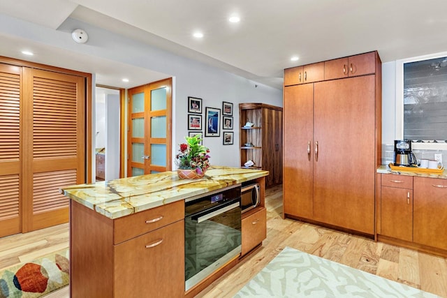 kitchen featuring appliances with stainless steel finishes, light hardwood / wood-style flooring, and light stone countertops