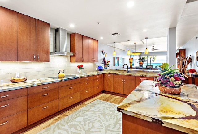 kitchen featuring wall chimney exhaust hood, hanging light fixtures, kitchen peninsula, sink, and light wood-type flooring