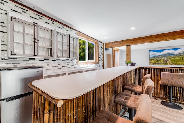 kitchen with wood finished floors, decorative backsplash, beam ceiling, freestanding refrigerator, and glass insert cabinets