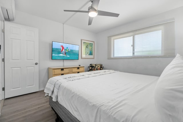 bedroom with a wall mounted AC, ceiling fan, and wood-type flooring