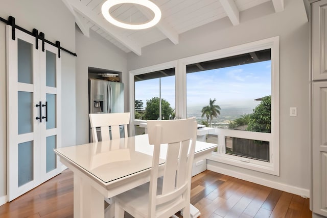dining room with baseboards, lofted ceiling with beams, a barn door, and wood finished floors