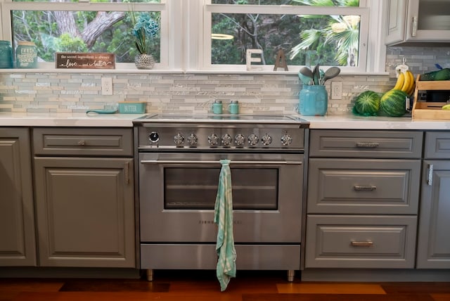kitchen with gray cabinetry, high end range, light countertops, and backsplash