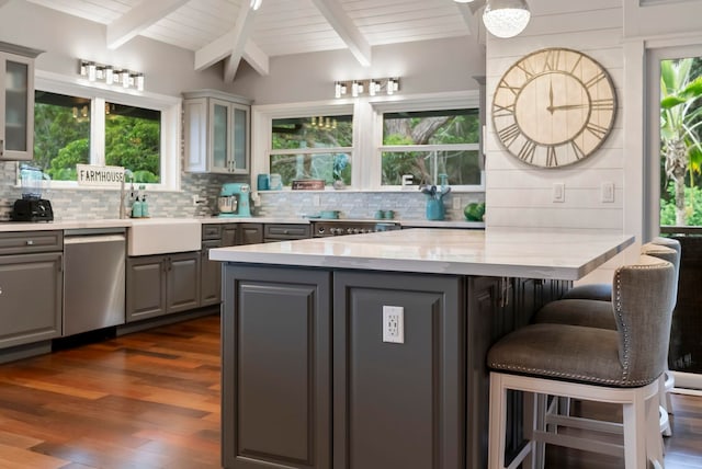 kitchen featuring backsplash, a breakfast bar area, stainless steel dishwasher, gray cabinetry, and dark wood finished floors