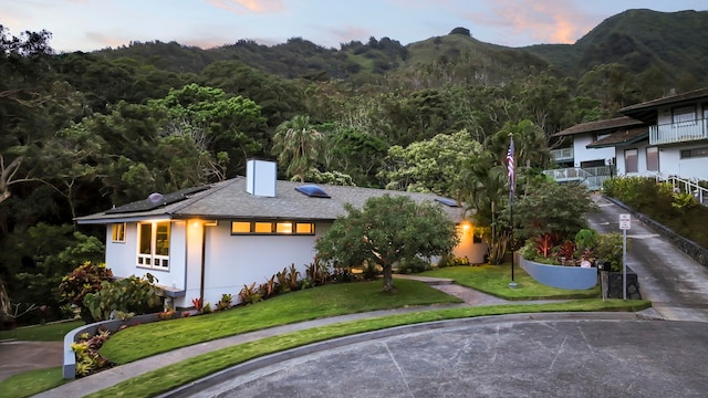 view of front facade featuring a chimney, stucco siding, a mountain view, a front lawn, and roof mounted solar panels