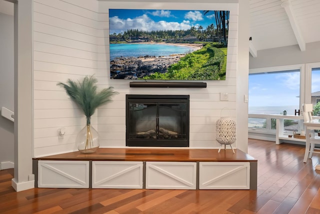 living room with a glass covered fireplace, vaulted ceiling with beams, and wood finished floors