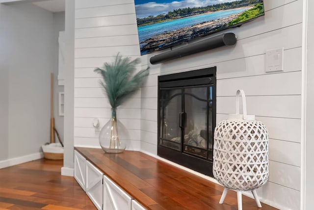room details featuring baseboards, wood finished floors, and a glass covered fireplace