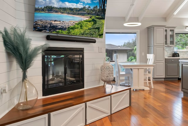 interior space featuring beam ceiling, light wood-style flooring, plenty of natural light, and a glass covered fireplace