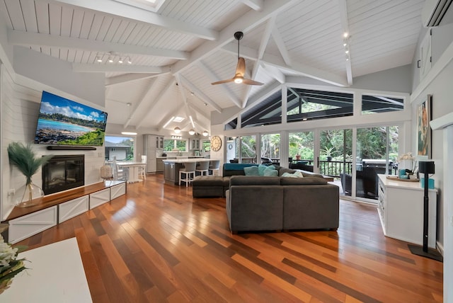 living room featuring high vaulted ceiling, a glass covered fireplace, a wall unit AC, and wood finished floors
