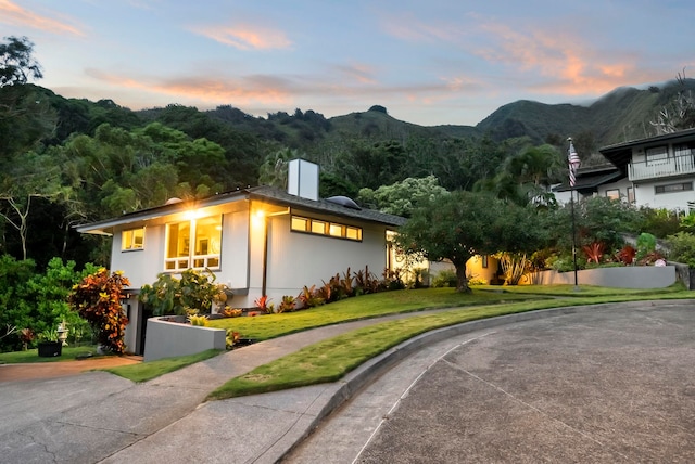 view of front of home featuring a chimney, a mountain view, a front lawn, and curved driveway
