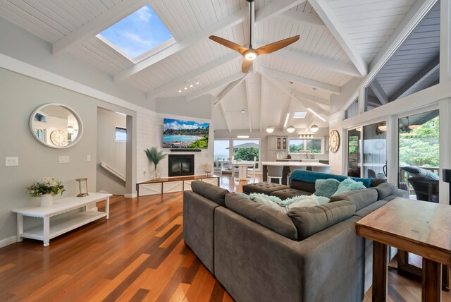living room featuring a glass covered fireplace, a healthy amount of sunlight, beam ceiling, and wood finished floors