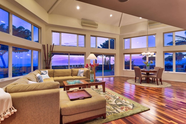 living room with dark hardwood / wood-style flooring, a wealth of natural light, a chandelier, a wall mounted air conditioner, and a towering ceiling