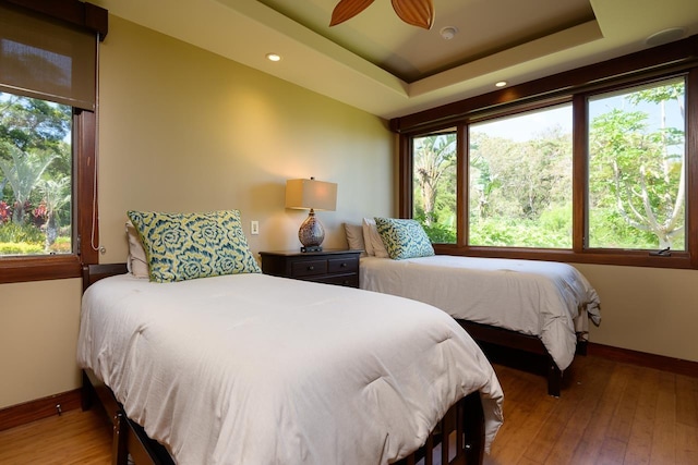 bedroom featuring baseboards, hardwood / wood-style floors, a raised ceiling, recessed lighting, and a ceiling fan