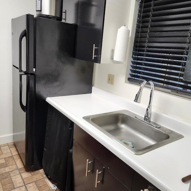 kitchen featuring dark brown cabinetry, sink, and black refrigerator