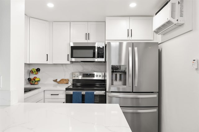 kitchen with appliances with stainless steel finishes, white cabinetry, light stone counters, and backsplash