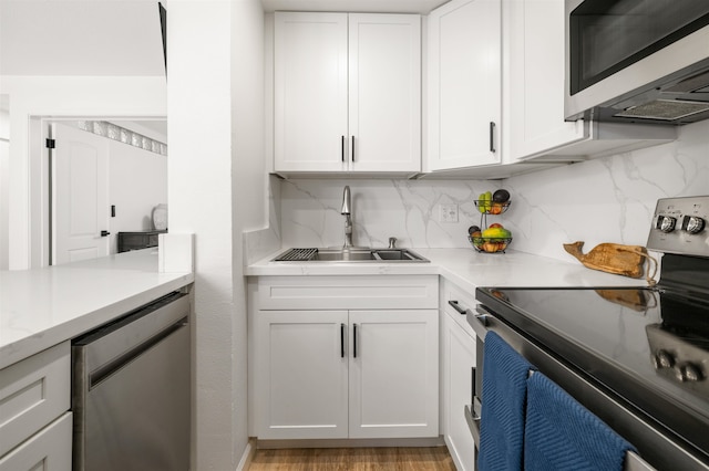 kitchen with sink, white cabinetry, stainless steel appliances, decorative backsplash, and light hardwood / wood-style flooring