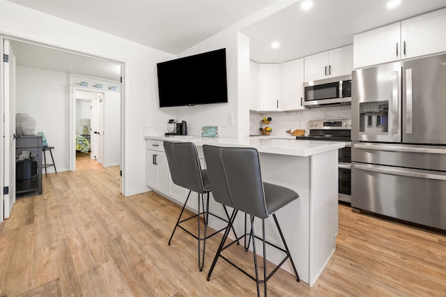 kitchen with white cabinets, a kitchen bar, stainless steel appliances, and light hardwood / wood-style floors