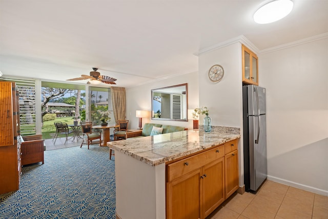 kitchen with light tile patterned floors, freestanding refrigerator, a peninsula, light stone countertops, and crown molding