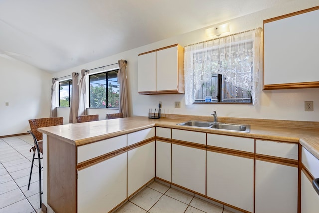 kitchen featuring lofted ceiling, kitchen peninsula, sink, white cabinetry, and light tile patterned floors