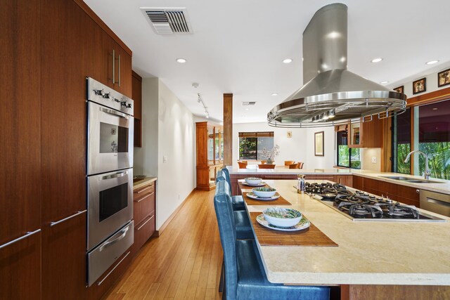 563 Mikioi Pl, Kihei, HI 96753 - kitchen with stainless steel double oven, island exhaust hood, gas cooktop, a warming drawer, and light wood-type flooring