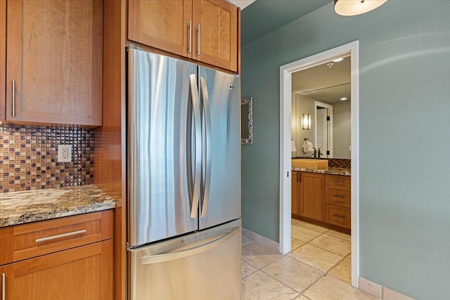 kitchen featuring light stone countertops, stainless steel fridge, and decorative backsplash