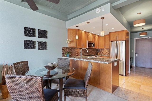 kitchen featuring kitchen peninsula, stainless steel appliances, light stone counters, and hanging light fixtures